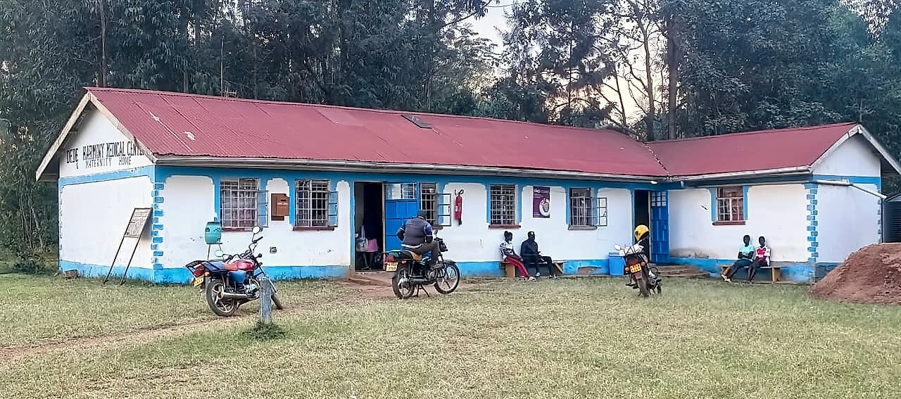 Dede Harmony Medical Centre & Maternity Home building — white walls with light blue trim, blue doors, red iron roof